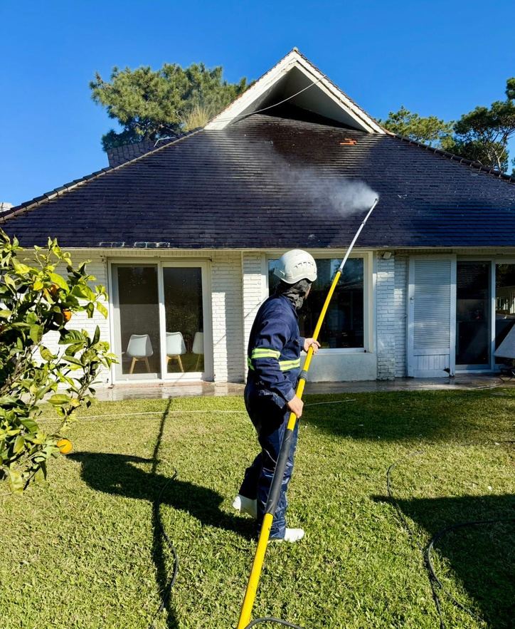 Operario hidrolavando el techo de una casa con una lanza extensible